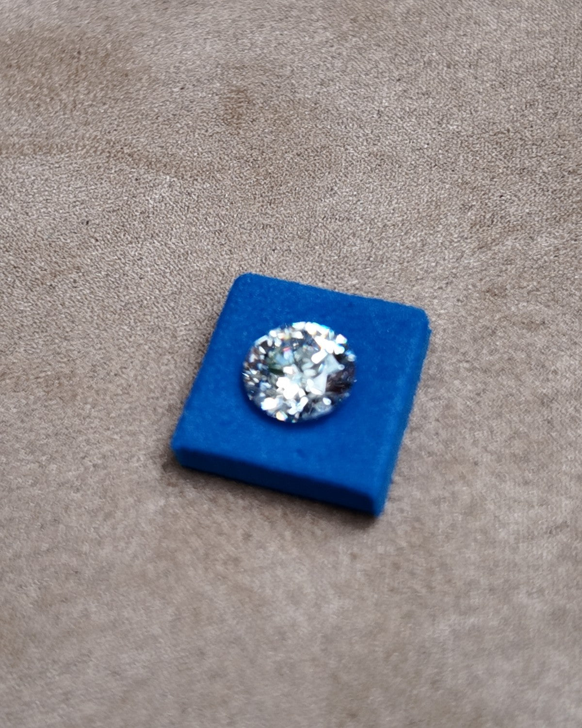 A loose round diamond seated in a blue stone pad on a jeweller's tray