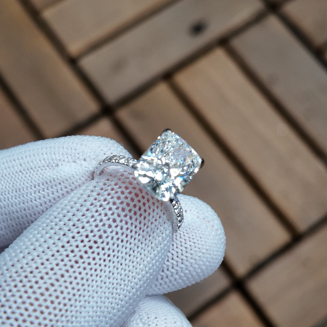 A cushion-cut diamond solitaire held in a gloved hand