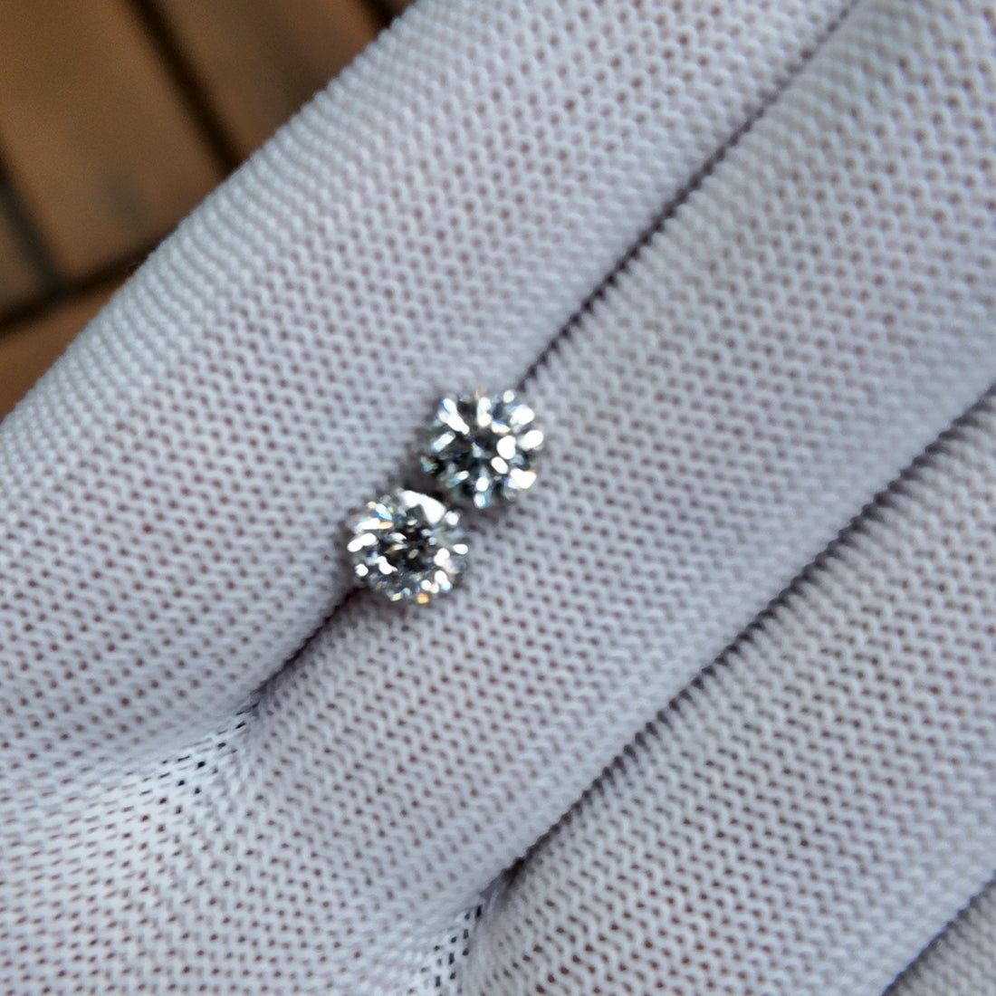 Two round diamond studs held on a gloved hand