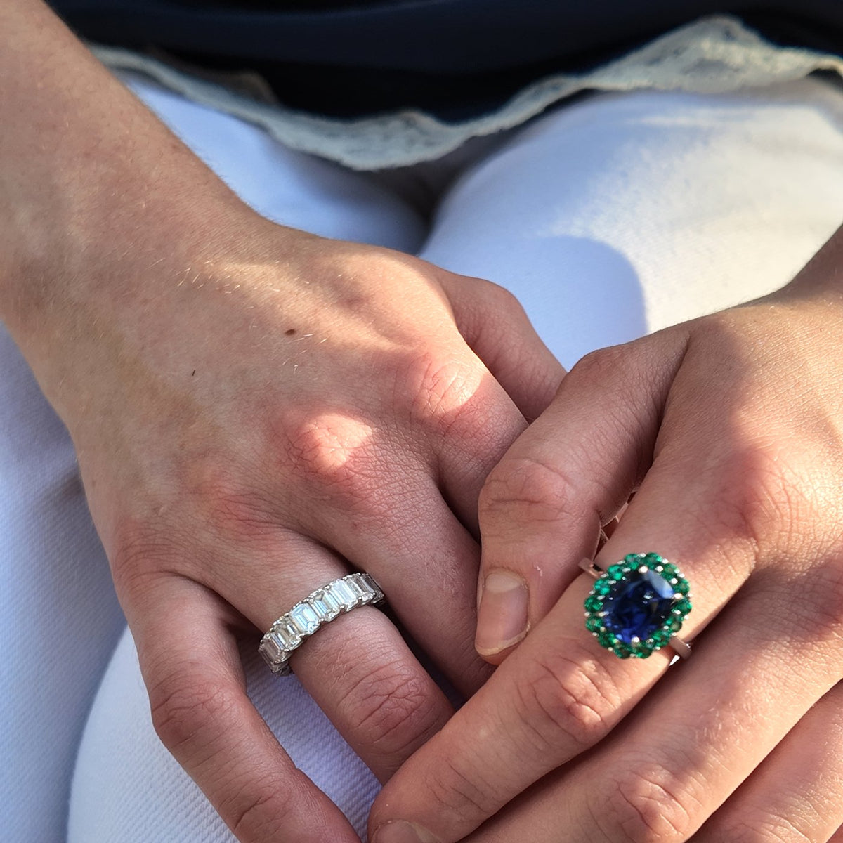 A blue sapphire ring with a green emerald halo, worn with a diamond eternity band