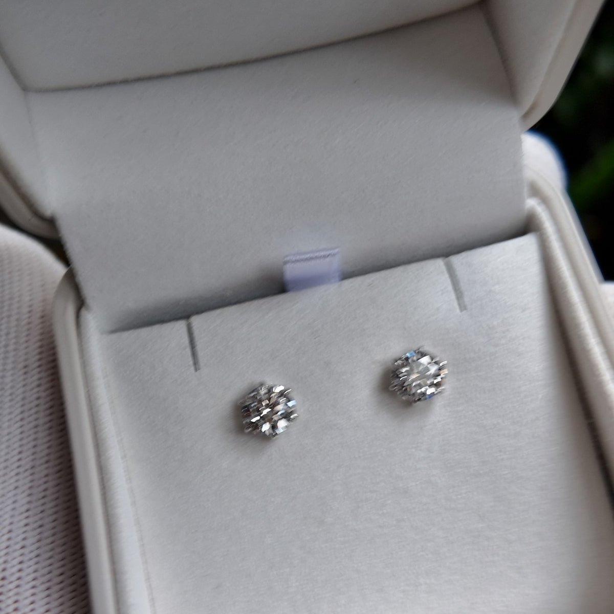 A pair of diamond stud earrings in an open Irdoja box