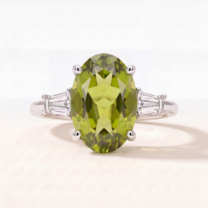 Oval peridot ring with tapered baguette diamond shoulders in platinum, studio view