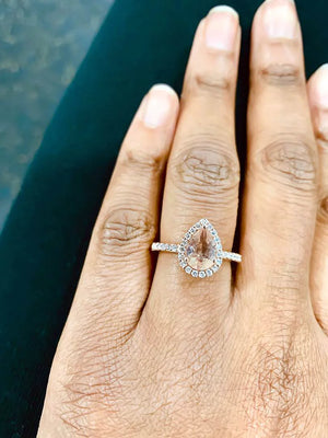 Prong-set pear morganite ring with diamond halo on hand, featuring 14k gold band and elegant design by Irdoja Diamonds.