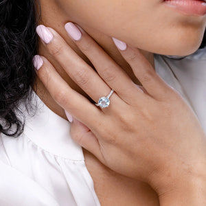 Aquamarine solitaire engagement ring with diamond accents set in 18k gold, worn on a hand with elegant nails.