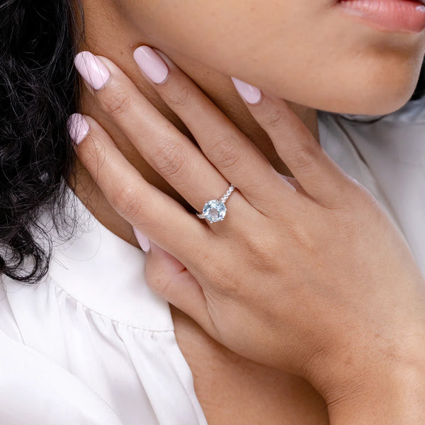 Aquamarine solitaire engagement ring with diamond accents set in 18k gold, worn on a hand with elegant nails.