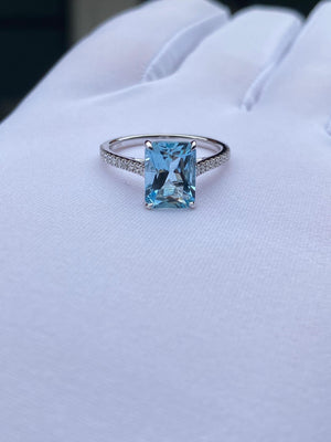 Emerald-Cut Aquamarine Ring with Diamond Band displayed on a hand, featuring an icy-blue center stone and sparkling diamond accents.