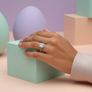 Emerald-Cut Aquamarine Ring with Diamond Band displayed on hand with pastel geometric background.