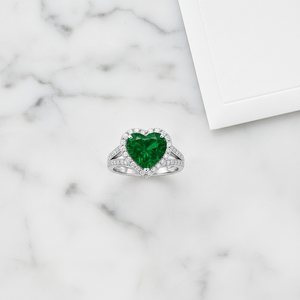 Heart-Shaped Lab Emerald Engagement Ring with Diamond Halo on a marble surface, showcasing its elegance and sparkle.