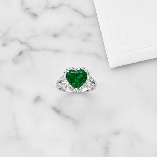 Heart-Shaped Lab Emerald Engagement Ring with Diamond Halo on a marble surface, showcasing its elegance and sparkle.