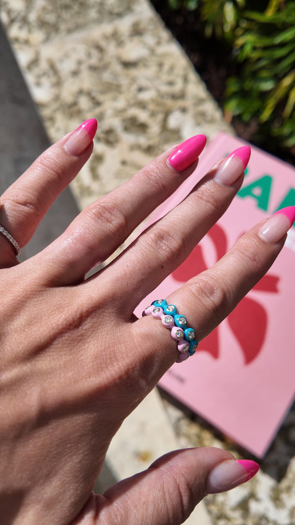 Two Irdoja Bubble bands stacked on one finger, pink and teal enamel with bezel-set stones, worn in daylight.
