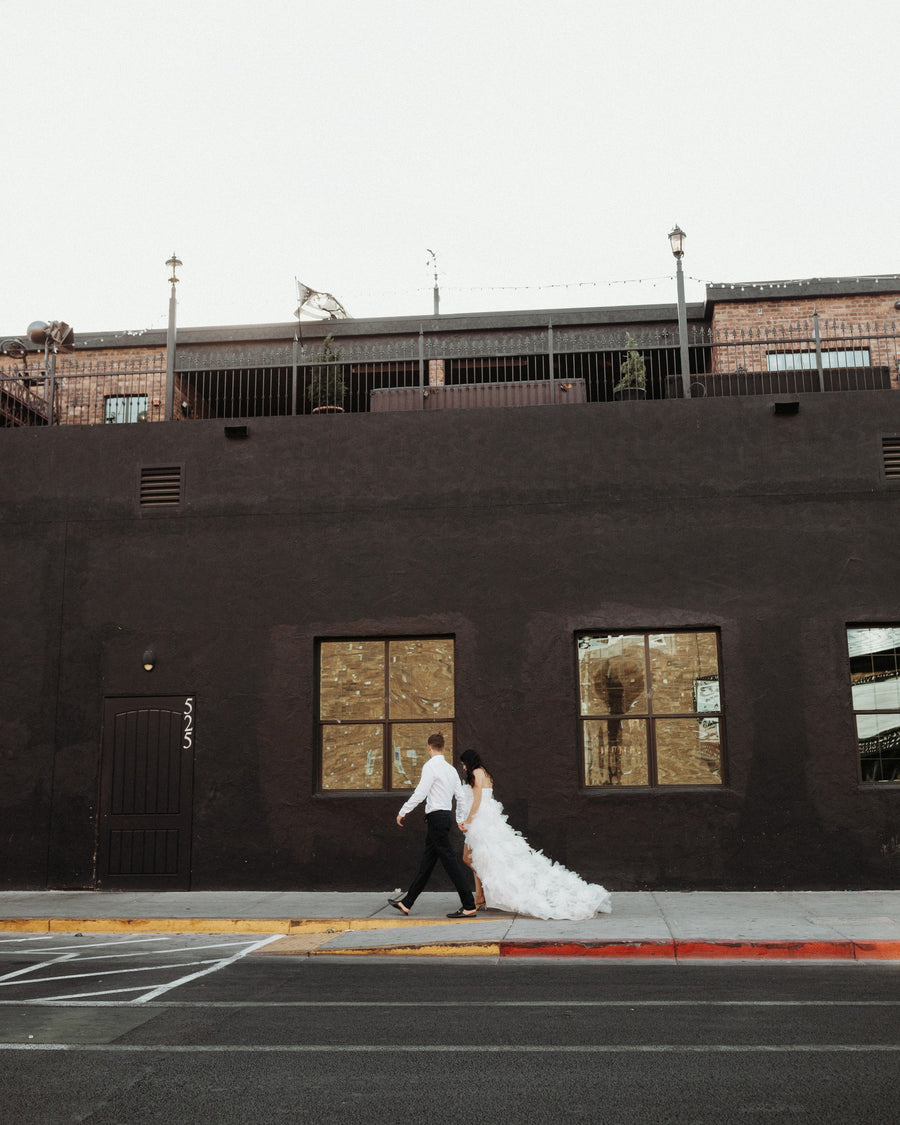 A bride and groom crossing a street, the bride's train trailing behind