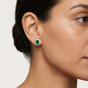 Woman wearing Lab-Grown Emerald Halo Stud Earrings with Diamonds featuring a green oval-cut emerald surrounded by diamonds.