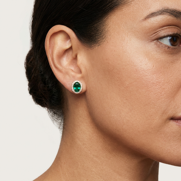 Woman wearing Lab-Grown Emerald Halo Stud Earrings with Diamonds featuring a green oval-cut emerald surrounded by diamonds.