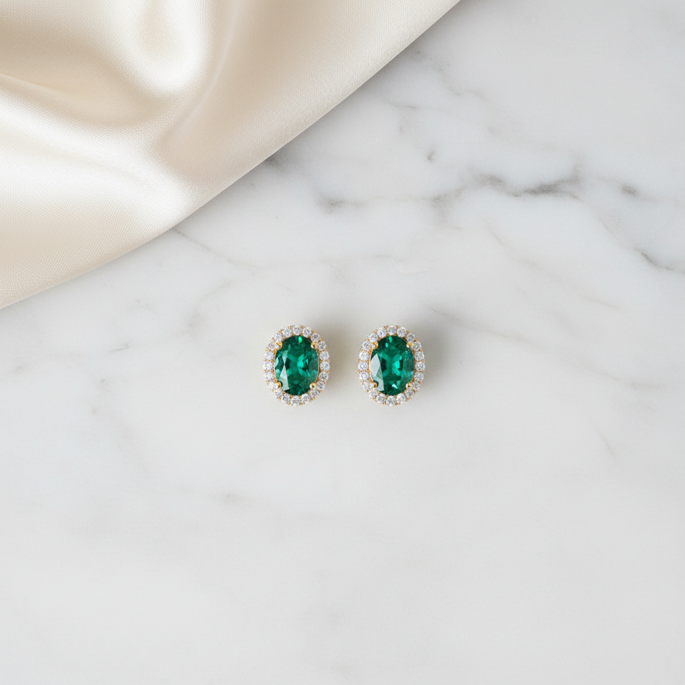 Model wearing Lab-Grown Emerald Halo Stud Earrings with Diamonds, showcasing elegance and vibrant color next to a sheer curtain.