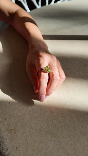 Oval peridot ring in platinum, worn on a sunlit ledge