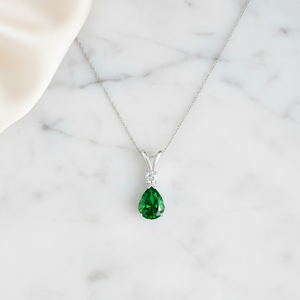 Prong-Set Lab-Grown Emerald Teardrop V-Bale Pendant with Diamond on marble background.