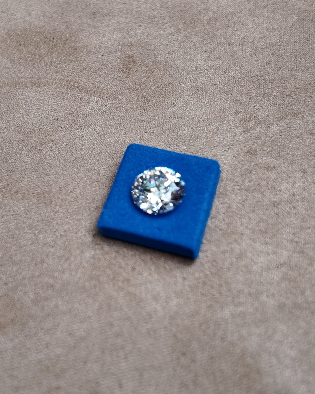 A loose round diamond seated in a blue stone pad on a jeweller's tray